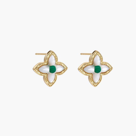 Gold quatrefoil stud earrings with white mother-of-pearl petals and emerald green gemstone center on beige background.