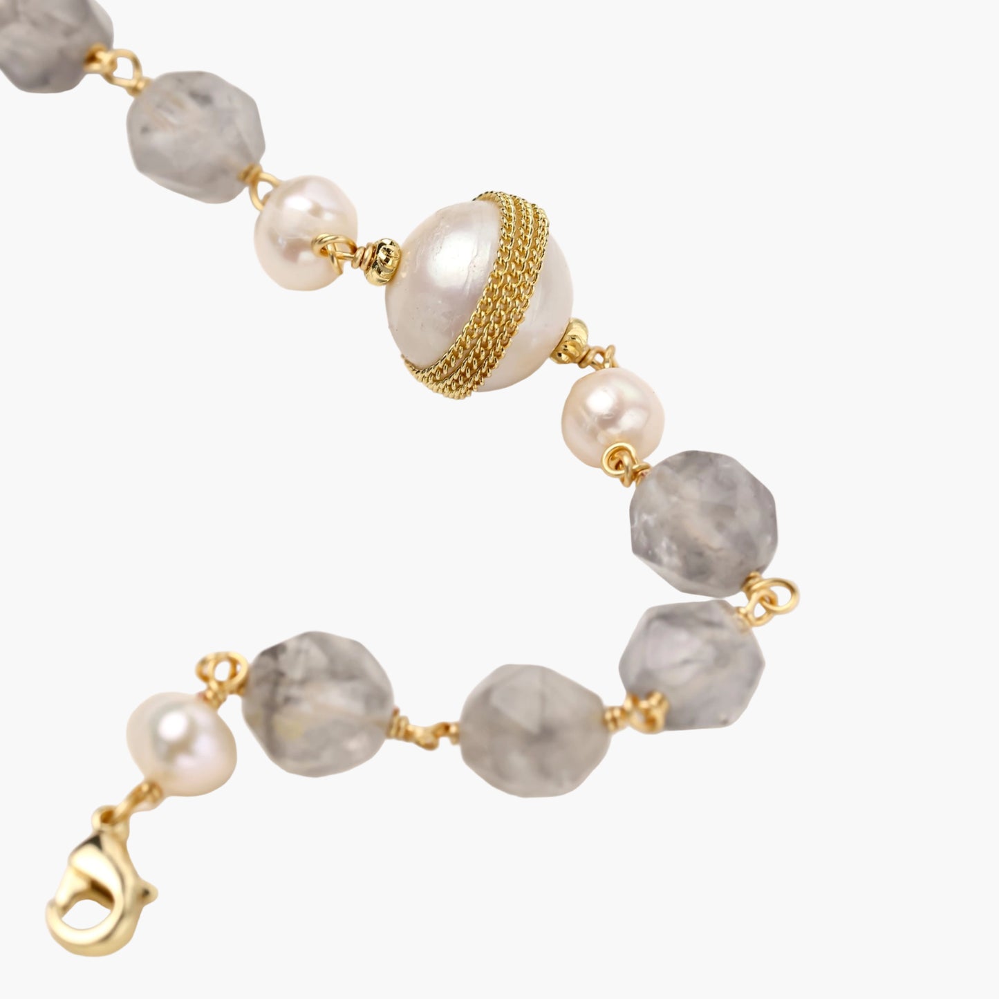 Bracelet with cloudy quartz beads, freshwater pearls, and gold-wrapped baroque pearl centerpiece on white background.