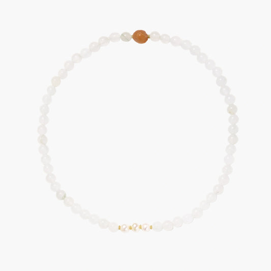 Three layered white beaded bracelets with carved orange agate lotus centerpiece and freshwater pearls on cream background.