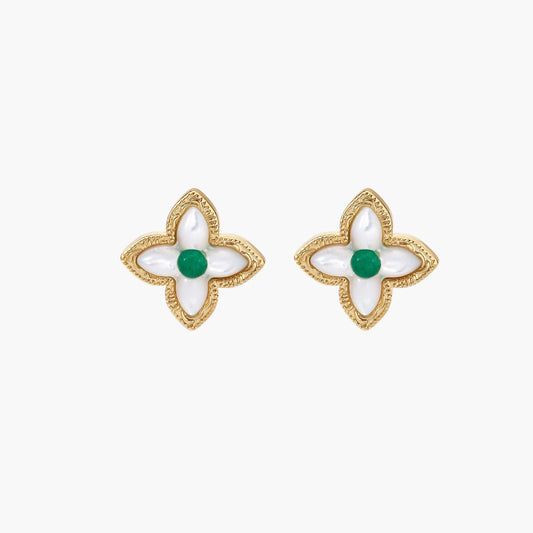 Gold quatrefoil stud earrings with white mother-of-pearl petals and emerald green gemstone center on beige background.