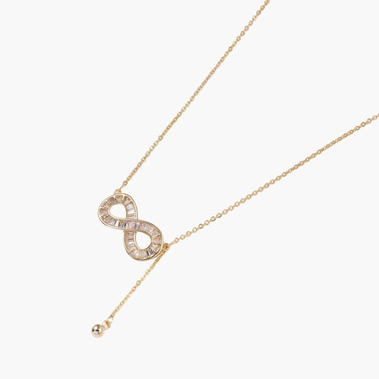 Gold infinity pendant with baguette crystals on adjustable chain against cream background.