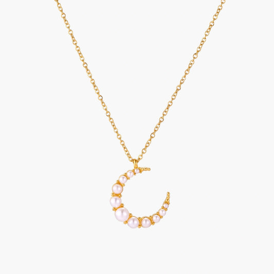 Gold crescent moon pendant with graduated white pearls on delicate chain against cream background